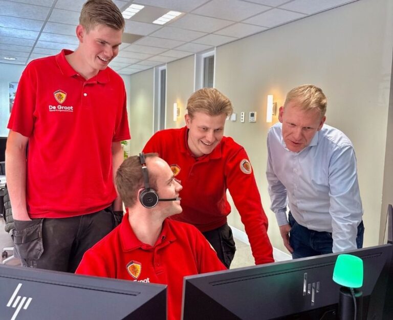 Vier collega's staan samen bij computer en overleggen en lachen.