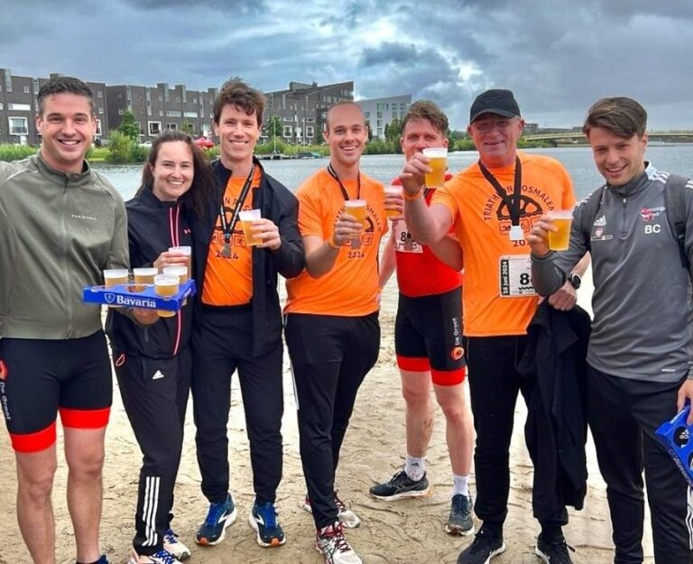 7 collega's staan bij sportevenement met drinken in hun hand.