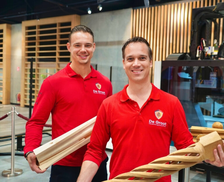 Twee collega's van De Groot staan bij cnc-machine met houtproducten in de hand.