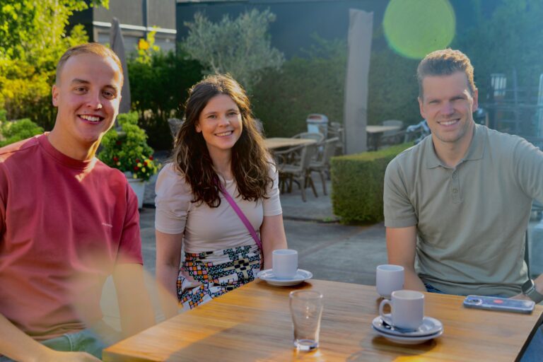 Drie collega's lachen tijdens ontbijt bij bedrijfsfeest.
