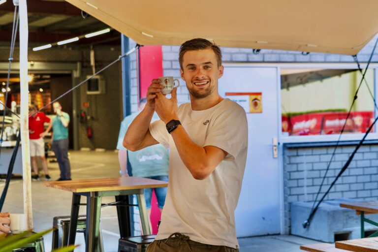 Collega staat tijdens bedrijfsfeest buiten met een koffiekopje in zijn hand.