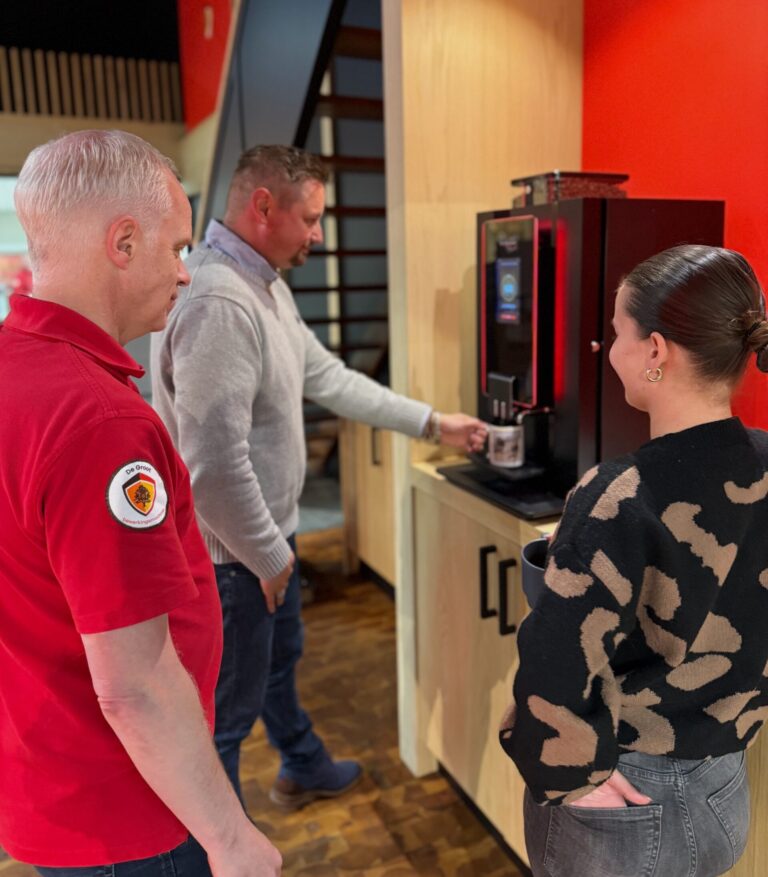 Drie collega's staan bij koffieautomaat te kletsen.