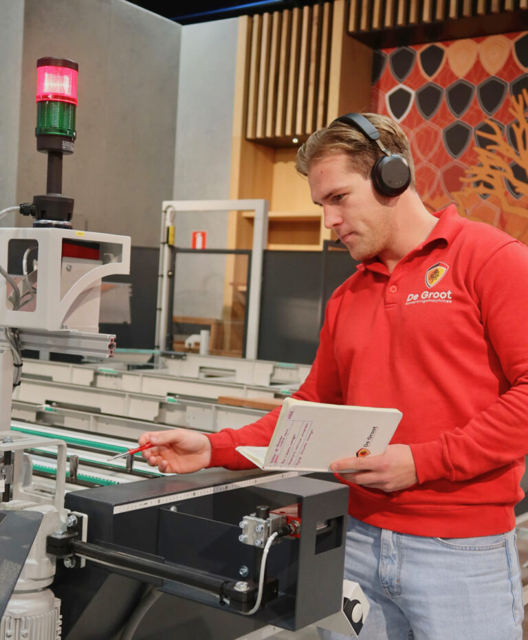 Servicecenter technici De Groot wijst naar machine met pen met koptelefoon op